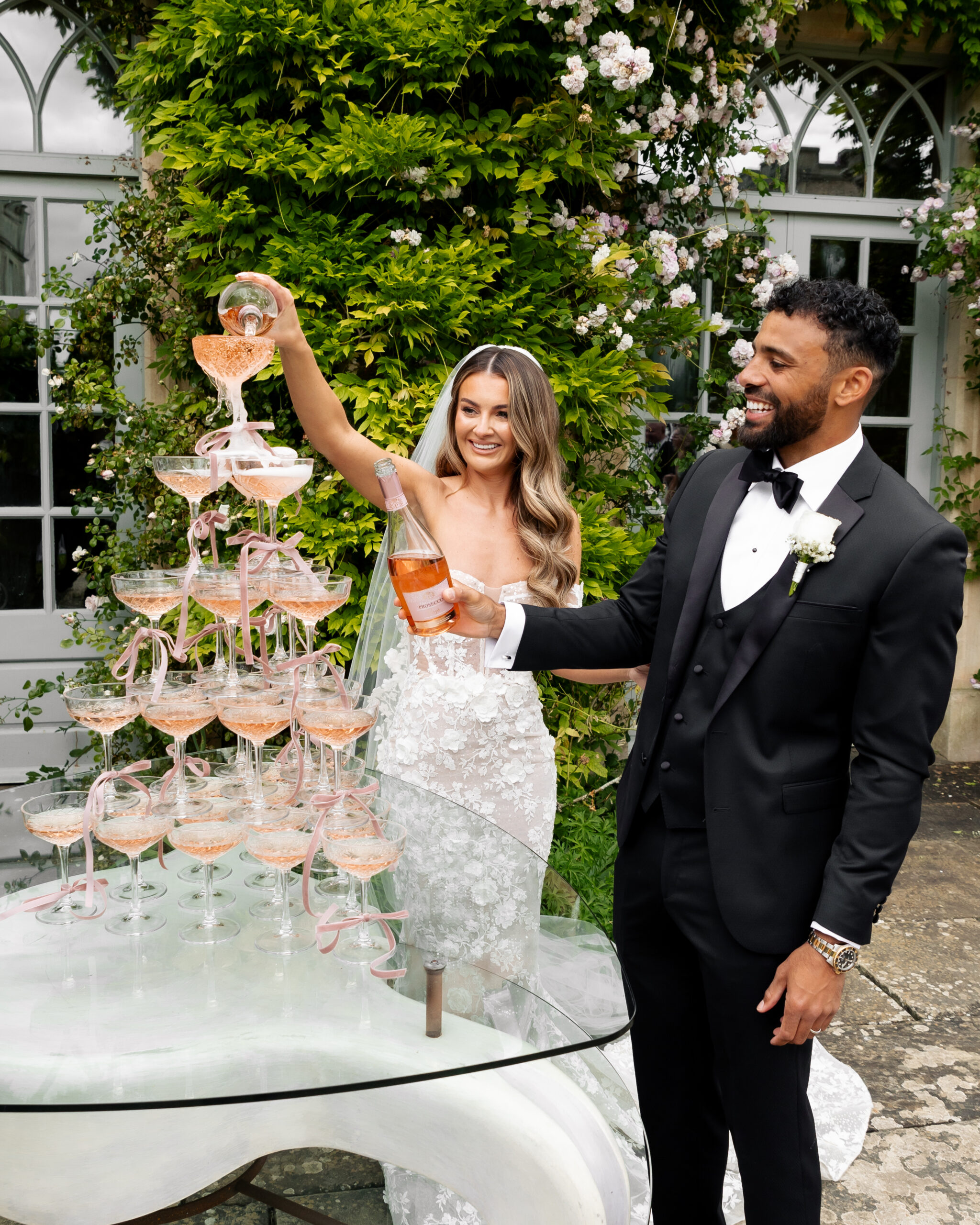 A couple on their wedding day at Euridge Manor, pouring champagne from a champagne tower to celebrate being married the bride wears a stunning Berta gown and the groom is in black tie tuxedo